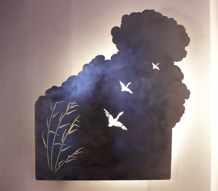 Wandleuchte mit Gänsen, die über einen Teich in die Wolken fliegen